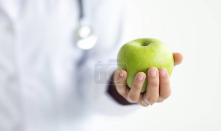 Photo for Healthy food, diet, nutrition concept. Cropped of woman wearing medical coat doctor dietitian nutritionist holding fresh organic green apple in her hand, white background, banner - Royalty Free Image