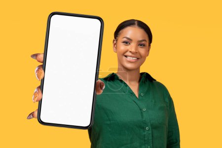 Foto de Pago en línea, Banca, Compras. Mujer negro sonriente en Casual Mostrando Smartphone grande con blanco pantalla en blanco Mockup posando sobre fondo amarillo, mirando a la cámara. Aplicación móvil - Imagen libre de derechos