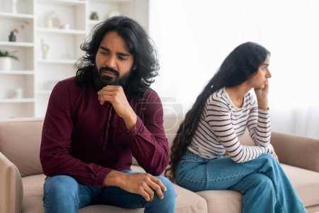 Photo for Upset indian couple having fight at home, unhappy young man and woman sitting on couch far from each other, looking aside, thinking about divorce, cant solve conflict, breakup after quarrel - Royalty Free Image
