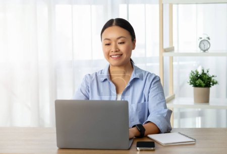 Photo for Millennial Asian woman wearing casual clothing freelancer working from home, sitting on desk, typing on laptop, copy space. Remote job, freelance, work in IT - Royalty Free Image