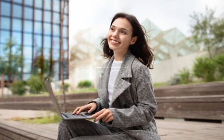 Photo for Happy European business lady using laptop computer outside in urban city area, smiling to camera as she typing and browsing internet, working online. Digital work and modern lifestyle - Royalty Free Image