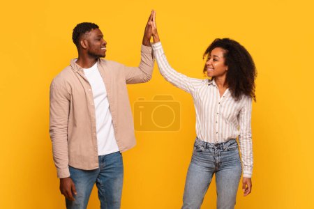 Foto de Pareja afroamericana alegremente chocándose los unos a los otros, celebrando el momento de éxito con sonrisas genuinas, sobre un fondo amarillo vivo - Imagen libre de derechos