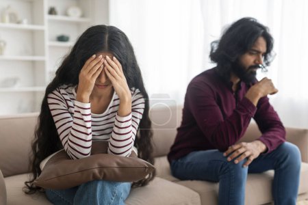 Photo for Frustrated young indian couple sitting on couch after quarrel at home. Unhappy millennial spouses experiencing difficulties crisis in marriage, have fight, living room interior - Royalty Free Image