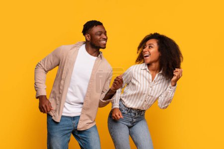 Photo for Joyous African American couple sharing dance move, laughing heartily with genuine happiness and connection, set against vibrant yellow background - Royalty Free Image