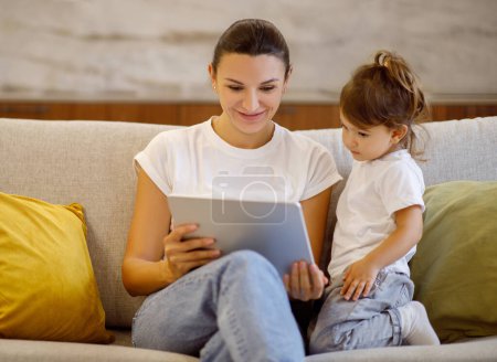 Photo for Mom and cute little daughter using digital tablet together at home, focused mother and curious preschool female child sitting on couch, engrossed in educational app on modern gadget, closeup - Royalty Free Image
