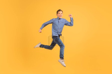 Foto de Dinámico adolescente saltando en el aire contra el fondo del estudio amarillo, feliz adolescente masculino irradiando alegría y energía, encapsulando la esencia de la libertad y la felicidad en la juventud, espacio de copia - Imagen libre de derechos