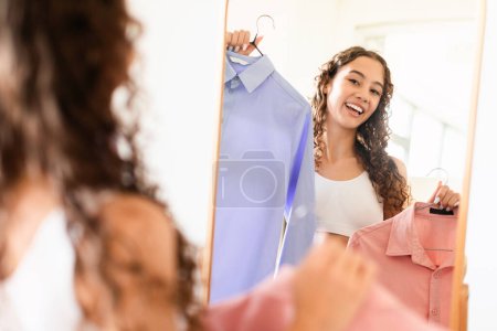 Compras, moda femenina. alegre adolescente chica elegir ropa y trajes cerca de espejo en casa. Estilo personal y concepto de compras. Enfoque selectivo, espacio vacío para el texto