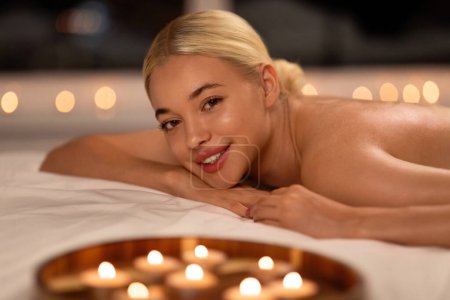 Photo for Massage And Wellness. Happy young blonde lady lying on massage desk after relaxing bodycare treatment, smiling to camera. Woman enjoying beauty care and pampering at luxury spa salon - Royalty Free Image