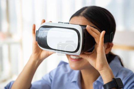 Modern rester à la maison passe temps. Gros plan positif dame asiatique en réalité virtuelle casque explorant le cyberespace à l'intérieur. Jeune coréenne en lunettes VR jouant jeu informatique interactif