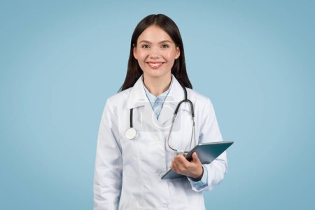 Nahbare Ärztin mit digitalem Tablet und warmem Lächeln, bereit für Telemedizin-Dienste, vor beruhigendem blauen Hintergrund