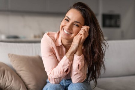 Photo for Radiant woman with contagious smile poses playfully, hands gently cradling her face, capturing moment of genuine happiness and effortless charm - Royalty Free Image
