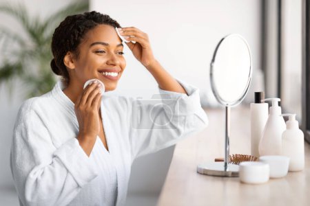 Photo for Attractive Black Woman Looking In Mirror And Cleansing Skin With Cotton Pads, Beautiful Smiling African American Female Making Daily Beauty Routine At Home, Enjoying Skincare Treatments, Closeup - Royalty Free Image