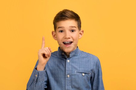 Idea Concept. Excited Teen Boy Pointing Finger Up And Looking At Camera, Teenage Male Child Having Eureka Moment While Standing Isolated Over Yellow Background In Studio, Copy Space
