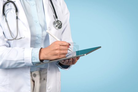 Nahaufnahme einer Ärztin, die auf einem digitalen Tablet schreibt und moderne Krankenakten mit Stethoskop vor blauem Hintergrund zeigt, ausgeschnitten