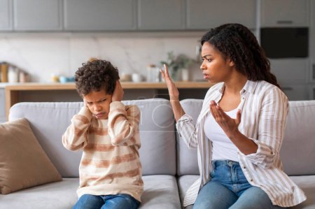 Photo for Stubborn Child. Offended black boy covering ears, not to hear mothers scolding, emotional african american woman arguing with her preteen son, family of two quarelling while sitting on couch at home - Royalty Free Image