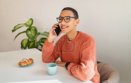 Photo for Happy millennial latin lady call by smartphone, drink cup of coffee, eat croissant, in modern cafe, office interior. Lunch, communication remotely, business conversation, work - Royalty Free Image