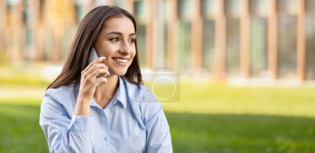 Téléchargez les photos : Joyeux jeune gestionnaire de femme caucasienne professionnelle ayant une conversation agréable sur son téléphone, avec un arrière-plan extérieur lumineux suggérant un environnement de travail détendu en ville - en image libre de droit