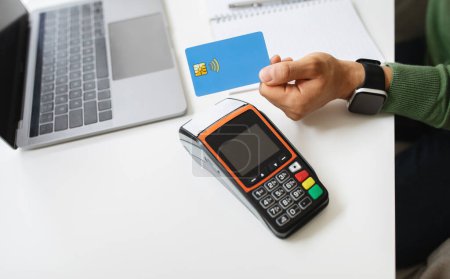 Photo for Customer using credit card for payment to owner at cafe restaurant, cashless technology and credit card payment concept. Cropped man hand holding bank card next to terminal, contactless payment - Royalty Free Image