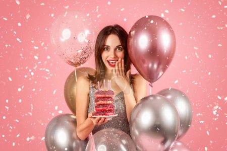 Photo for Cheerful surprised millennial caucasian woman in dress with many balloons hold cake with donuts, isolated on pink background, studio. Ad and offer, celebration holiday, birthday party with confetti - Royalty Free Image