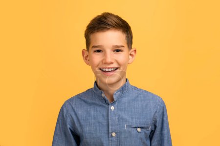 Téléchargez les photos : Adolescent beau garçon avec sourire heureux regardant la caméra, portrait d'adolescent souriant et joyeux portant une chemise en denim debout isolé sur fond jaune, exprimant des émotions positives, espace de copie - en image libre de droit