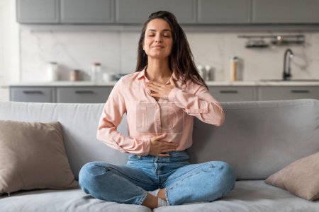 Photo for Content and serene woman enjoys moment of tranquility while meditating on her comfortable couch, epitomizing peaceful living in her modern home - Royalty Free Image
