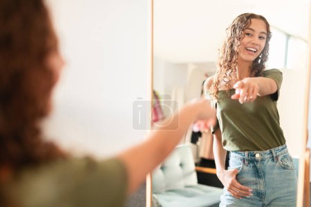 Téléchargez les photos : Adolescente caucasienne insouciante avec une silhouette mince et saine debout à l'intérieur, se montrant dans un miroir à la maison, incarnant la confiance des adolescents, le bien-être et l'amour-propre. Concentration sélective - en image libre de droit