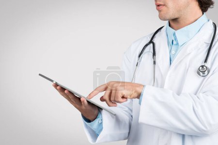 Partial profile of male doctor using digital tablet, focused on gadget, highlighting modern healthcare and medical technology use, cropped
