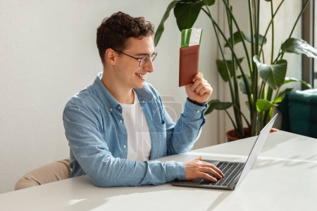 Photo for Cheerful millennial caucasian man student in glasses, use computer for video call, show passport and tickets in cafe. Travel for weekend, holiday, tourism and rest, journey - Royalty Free Image