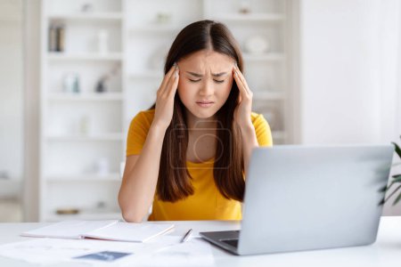 Téléchargez les photos : Stressé jeune asiatique femme pigiste ayant mal à la tête tout en travaillant au bureau à domicile, Millennial Korean Woman souffrant de migraine aiguë, Frotter les temples et froncer les sourcils, Copier - en image libre de droit