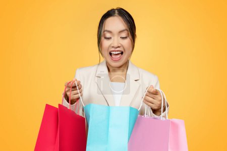 Überrascht, froh, junge koreanische Ladys Shopaholic öffnen bunte Taschen, mit Einkäufen genießen Einkaufen, isoliert auf orangefarbenem Studiohintergrund. Großer Verkauf, Mode, Geschenke und Neueinkäufe