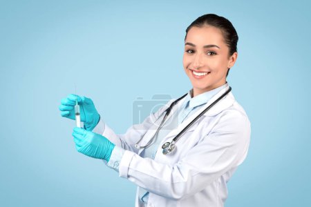 Photo for Cheerful female doctor in lab coat drawing medicine into syringe, ready for patient care, symbolizing trust in medical procedures, blue background - Royalty Free Image