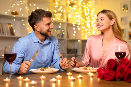 Téléchargez les photos : Couple joyeux partageant rire autour d'un dîner romantique avec du vin rouge, des pâtes et un bouquet de roses, illuminé par des chandelles chaudes, profiter de la soirée - en image libre de droit
