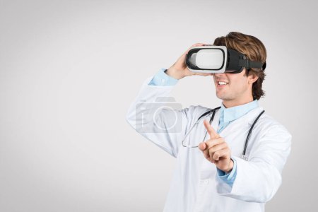 Photo for Enthusiastic male doctor wearing virtual reality headset, pointing and interacting with digital content, illustrating advanced medical training or treatment simulation - Royalty Free Image
