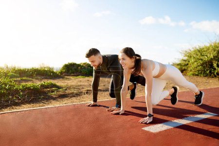 Energetic young couple in sportswear on starting blocks, poised to sprint on running track, reflecting competition and healthy lifestyle, free space