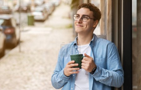 Photo for Glad calm european young man student in glasses drink tea, enjoy coffee cup, peace, look at free space in modern cafe, outdoor. Break, routine breakfast in morning, lifestyle, spare time - Royalty Free Image