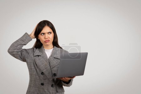 Téléchargez les photos : Femme d'affaires dans le blazer à dents de poule regardant confus et se grattant la tête tout en tenant un ordinateur portable, dépeignant la résolution de problèmes ou de doute, copier l'espace - en image libre de droit