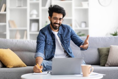 Photo for Distance Learning. Smiling Indian Male Attending Online Lesson, Having Video Call On Laptop With Teacher And Taking Notes At Home, Handsome Eastern Man Talking At Web Camera, Copy Space - Royalty Free Image