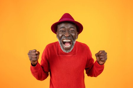 Téléchargez les photos : Joyeux vieil homme noir excité dans le chapeau, avec la bouche ouverte, crier, lever les poings, célébrer la victoire, le succès, isolé sur fond de studio orange. Vainqueur émotions, bonnes nouvelles, victoire - en image libre de droit