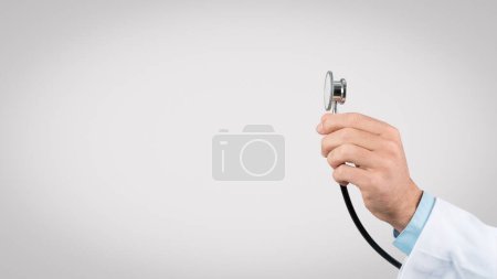 Close-up of medical professionals hand gripping stethoscope against plain grey background, depicting medical examination readiness