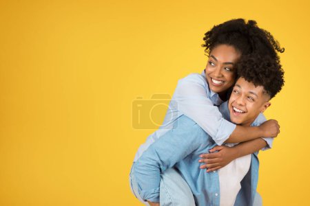 Glückliche junge afrikanisch-amerikanische Kerl hält Frau auf dem Rücken, haben Spaß, Blick auf leeren Raum, isoliert auf orangefarbenem Hintergrund Studio. Positiver Lebensstil, Liebe, Romantik und Beziehung