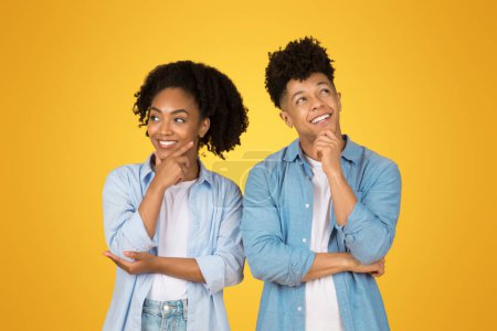 Photo for Smiling pensive young african american guy and woman in casual think, look at empty space, isolated on orange background studio. Positive lifestyle, question, choice together, sale - Royalty Free Image