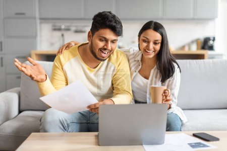 Photo for Happy Young Indian Spouses Making Video Call With Accountant While Using Laptop At Home, Joyful Eastern Husband And Wife Waving At Camera And Checking Financial Papers, Planning Family Budget - Royalty Free Image