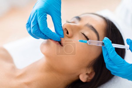 Photo for Beautician hands wearing gloves making beauty lips injection for beautiful young indian half-naked woman at beauty clinic, closeup shot. Aesthetic medicine concept - Royalty Free Image