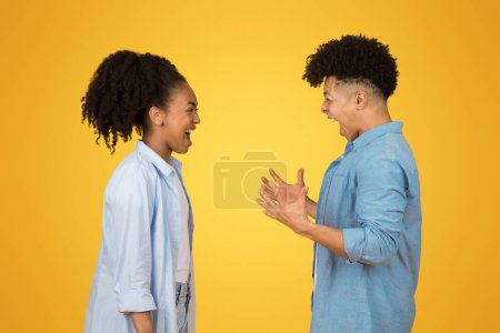 Angry young african american guy and woman in casual with open mouth, look at each other, scream, isolated on orange background studio. Quarrel, laud scandal, relationships problems