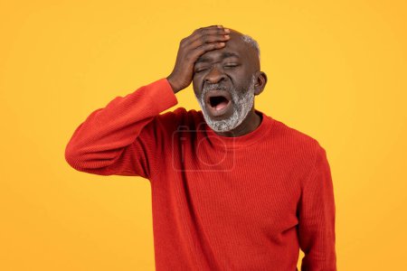 Foto de Angustiado anciano hombre negro con una barba blanca sosteniendo su cabeza en su mano, boca abierta en una expresión preocupada, usando un suéter rojo sobre un fondo amarillo liso - Imagen libre de derechos