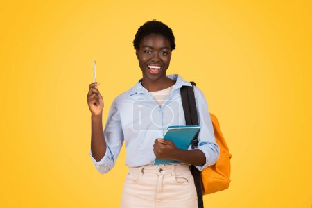 Photo for A black woman student, holding a pen, looks up thoughtfully, symbolizing a moment of inspiration or an idea, set against a bright yellow background that highlights her creativity and academic focus - Royalty Free Image