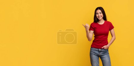 Foto de Cool feliz hermosa dama taiwanesa joven sosteniendo una mano en el bolsillo y apuntando al espacio de copia para la publicidad, mostrando mucho, buena oferta, aislado en el fondo de la pared amarilla, web-banner - Imagen libre de derechos