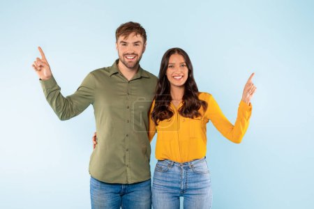 Photo for Happy man and woman with bright smiles, standing side by side and pointing upwards, suggesting shared goal or vision, against light blue backdrop - Royalty Free Image