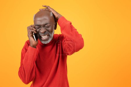 Photo for Distressed senior african american man in a red sweater, talking on a smartphone with a painful expression, clutching his head in frustration against a bright yellow background - Royalty Free Image