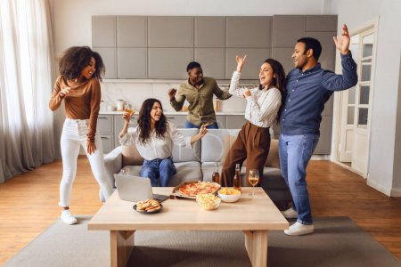 Téléchargez les photos : Groupe multiracial d'amis étudiants dansant en profitant d'une fête de week-end et dîner avec pizza et bière, riant ensemble dans un appartement moderne à l'intérieur, s'amusant pendant la célébration - en image libre de droit